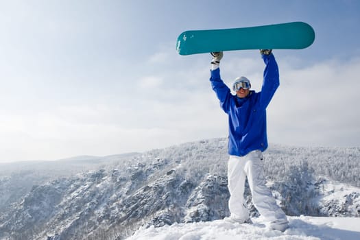 Portrait of joyful sportsman with snowboard standing on top of mount