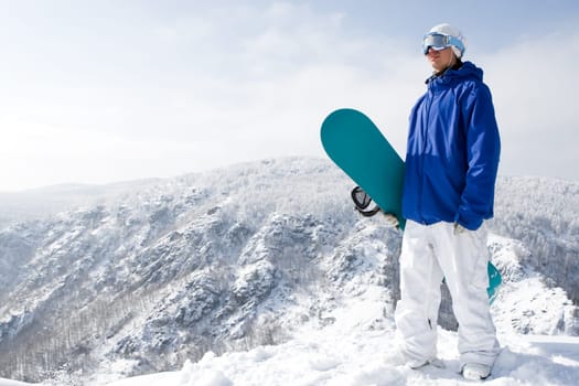 Portrait of happy sportsman with snowboard standing on top of mount