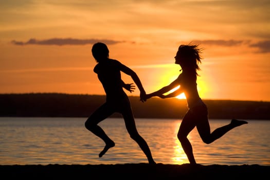 Silhouettes of happy couple having fun on seashore at sunset