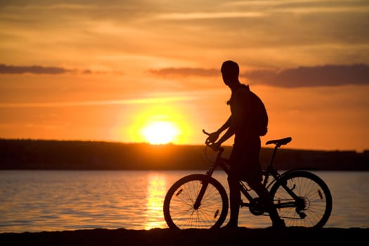 Silhouette of man riding bicycle with beautiful lake near by at sunset