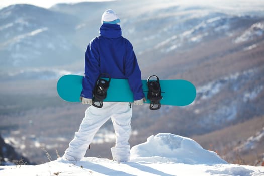 Rear view of sportsman with snowboard standing on top of mount