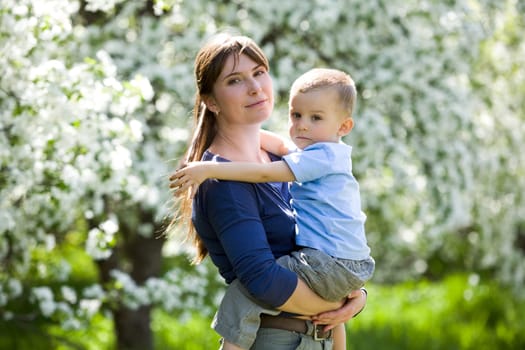 Portrait of pretty woman and her cute son looking at camera on background of blooming trees