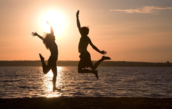 Silhouettes of happy couple jumping on background of lake at sunset