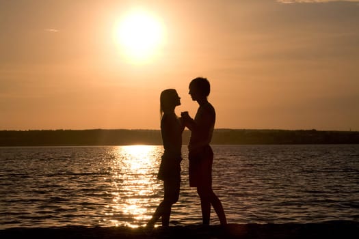 Profiles of romantic couple looking at each other on background of lake at sunset