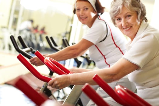 Portrait of two good-looking senior women training on exercise machines