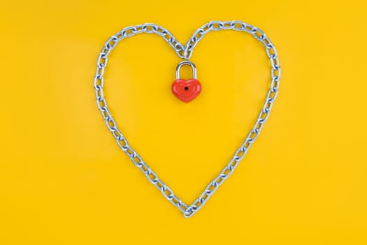 Image of metallic heart made of chain with lock on a yellow background