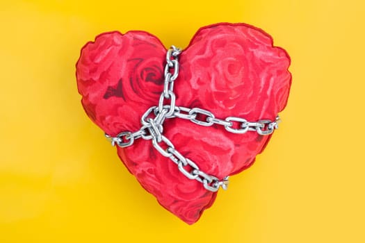 Image of toy heart held over by chain over yellow background