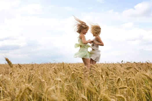Portrait of energetic twin sisters whirling in wheat field and having fun