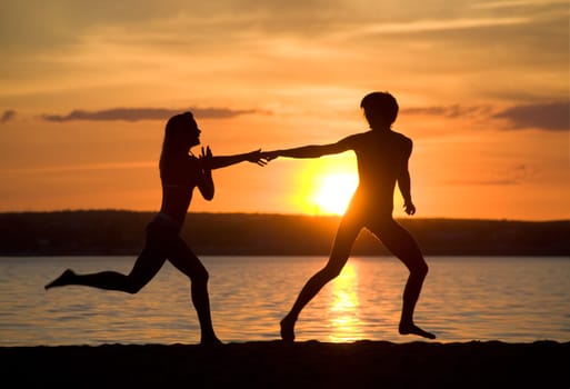 Silhouettes of happy couple running down seashore at sunset
