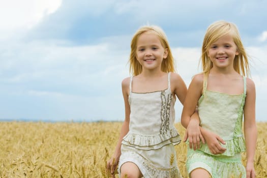 Portrait of cute twins walking down wheat field and smiling