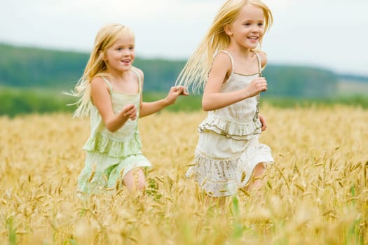 Portrait of happy girl running down wheat field with her twin sister behind