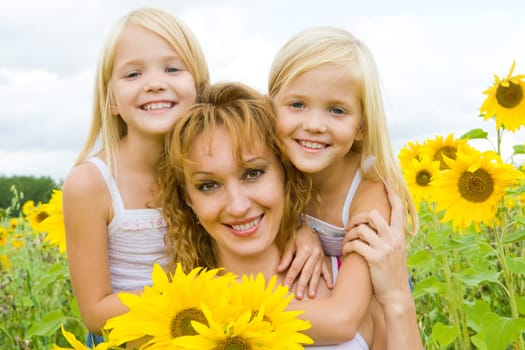 Portrait of cute twins embracing their mother with smiles in sunflower field