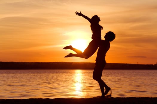 Figures of happy guy holding his girlfriend while the latter raising her arms at sunset