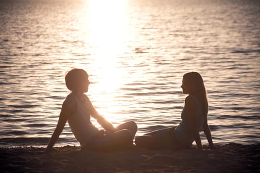 Photo of serene couple sitting on the seashore and talking at sunset