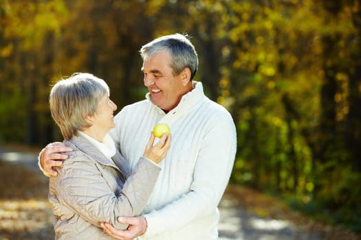 Photo of amorous aged man and woman holding apple and looking at each other