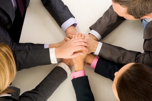 Image of business people keeping hands on top of each other at workplace