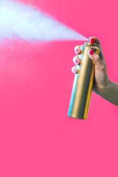 Photo of hair lacquer in females hand spraying it over red background