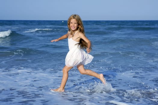 Little girl running beach shore splashing water in blue sea