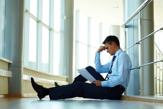 Portrait of serious businessman sitting on the floor while reading paper
