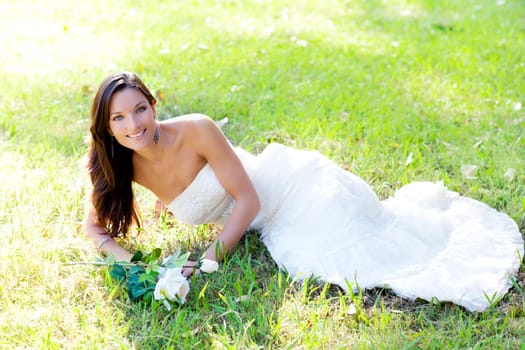 bride woman lying in park grass with white rose