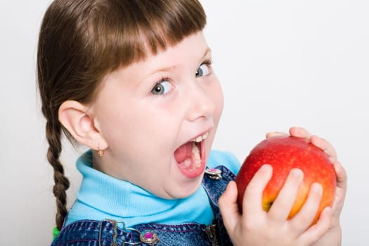 Cute girl looking aside with widely open mouth ready to eat red juicy apple