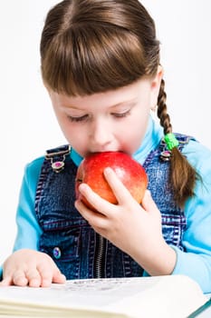 Photo of smart schoolgirl reading encyclopedia and eating apple