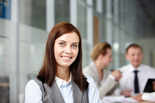 A beautiful businesswoman looking at camera with working partners behind