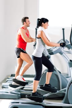 man and woman with elliptical cross trainer in sport fitness gym club