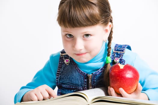 Portrait of little girl with red apple in hand and open book in front of her