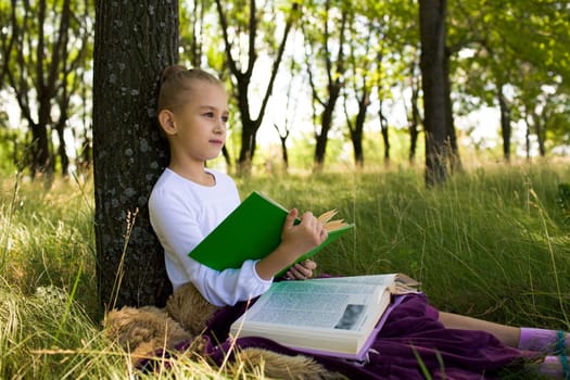 Pretty girl sitting under tree and thinking about something while reading books