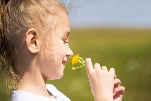 Fair-haired girl enjoying nice smell of yellow flower outdoors