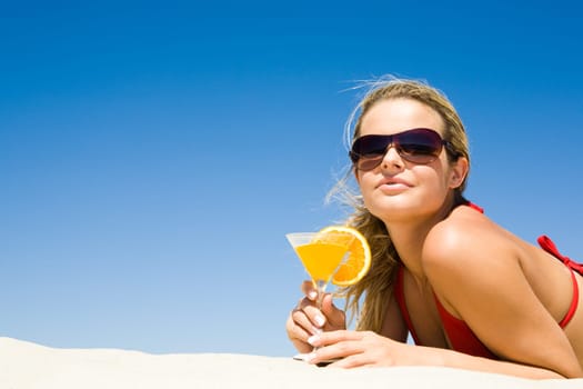 Portrait of relaxing woman wearing sunglasses with glass of cocktail in hand lying on sand
