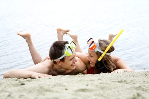 Portrait of cheerful couple in diving equipment lying on sandy shore
