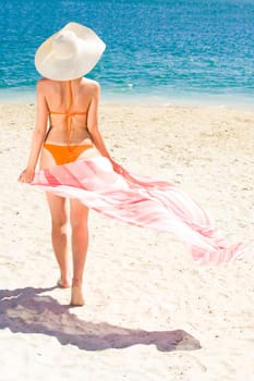 Portrait of woman with pareo walking aback along sandy beach during vacation