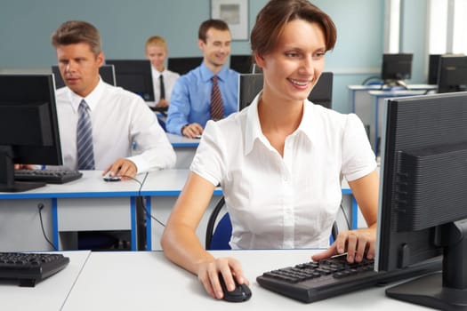 Businesspeople sitting at tables and looking at their monitors with smiling woman at foreground