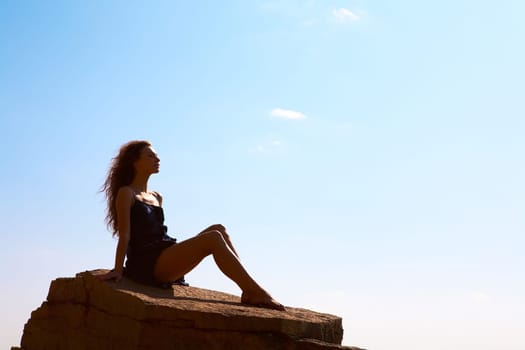 Photo of serene female seated on rock and relaxing
