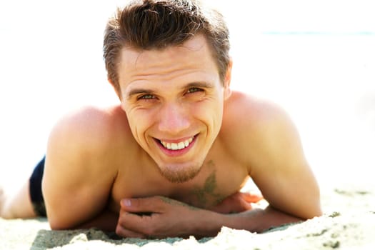 Photo of smiling guy lying on beach and looking at camera while sunbathing