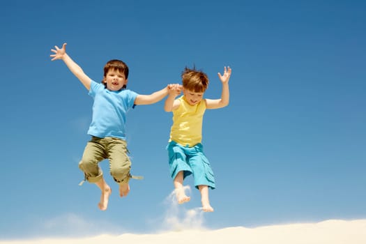 Photo of happy boys jumping on sandy beach and having fun