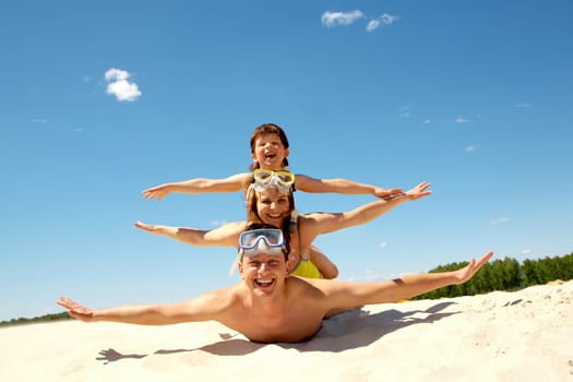 Portrait of cheerful couple and their son lying on sand and looking at camera