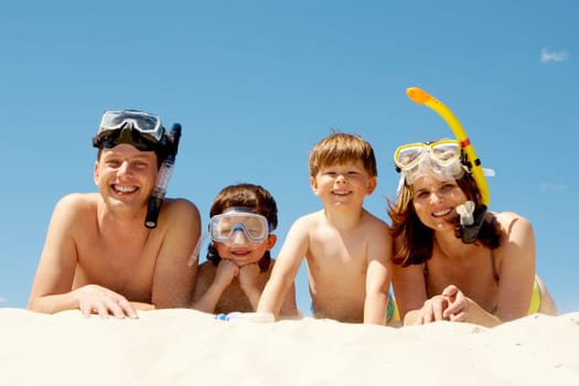 Portrait of diving family lying on sand against blue sky and smiling at camera