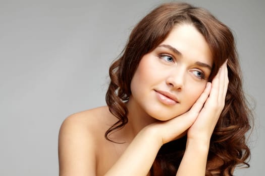 Fresh girl with hands by her cheek looking aside over grey background