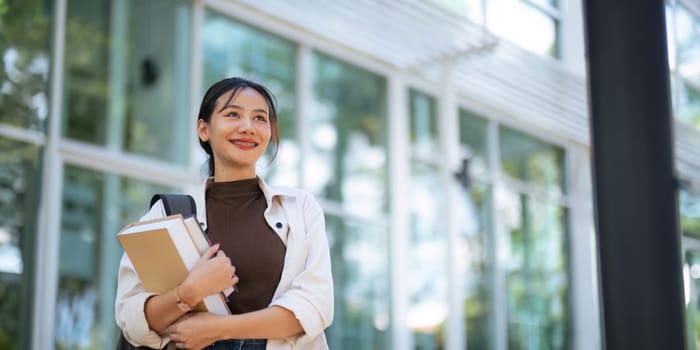 Beautiful young woman Asian with backpack and book. University student carrying lots of books in college campus. College and University life concept.