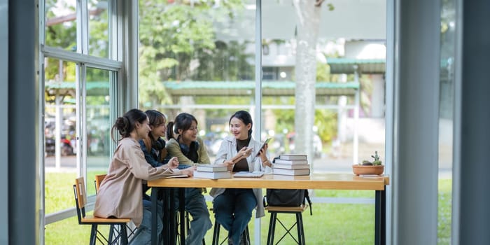 University students sitting together at table with book and laptop. Happy young people doing group study in college campus College and University life concept.