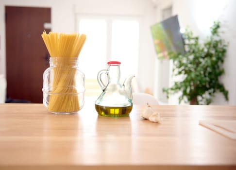 Front shot of a glass vintage bottle of fresh extra virgin olive oil and Italian spaghetti on the table in the home kitchen. Food and drink. Healthy organic food. Copy advertising space. Still life