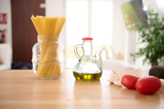 Still life. A glass oilcan of fresh extra virgin olive oil, Italian spaghetti and tomatoes on the table in home kitchen. Healthy eating. Italian cuisine