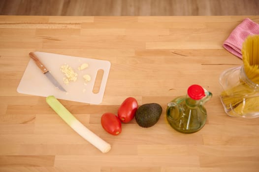 Top view of fresh vegetables, tomatoes, leek, avocado fruit and chopped garlic on the cutting board on the kitchen table. Healthy food. Dieting concept. Alimentation and nourishment. Copy ad space