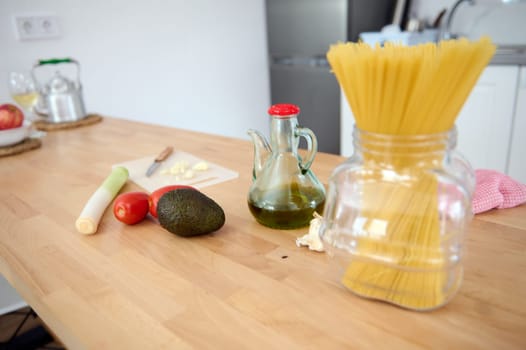 Food still life. Organic healthy raw vegan fruits and vegetables on a kitchen counter, oil can with extra virgin olive oil and Italian spaghetti. Organic ingredients for healthy dinner at home kitchen