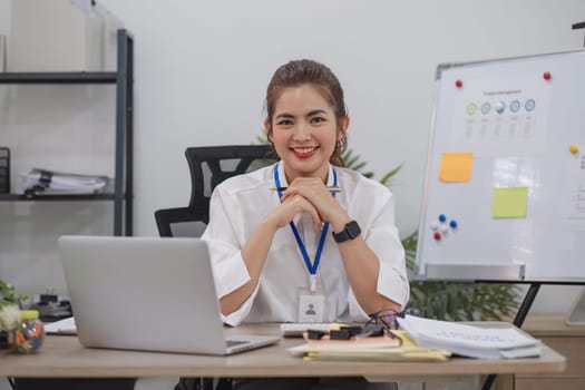 Charming Asian businesswoman working with a laptop at the office. Looking at camera..