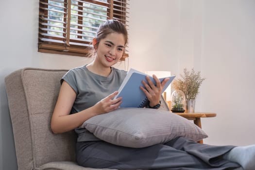 Happy young woman reading book on sofa at home. Lifestyle freelance relax in living room. Lifestyle Concept.