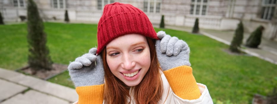 Cute girl student in red hat, warm gloves, sits in park, smiles and looks happy. Copy space